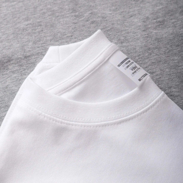 White oversized unisex cotton t-shirt with crew neckline and label detail lying on gray fabric.