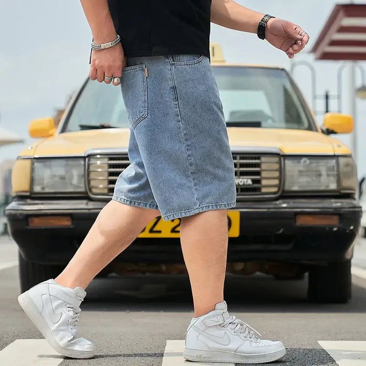 Men's plus size denim shorts in solid jeans color, showcasing casual summer style and comfort, with a person walking in front of a yellow car.